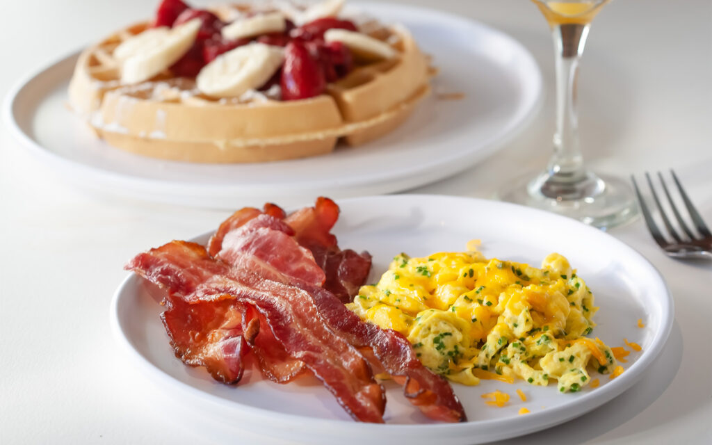 Focus on Bacon and Eggs on a Plate in Front of a Plate of Waffles
